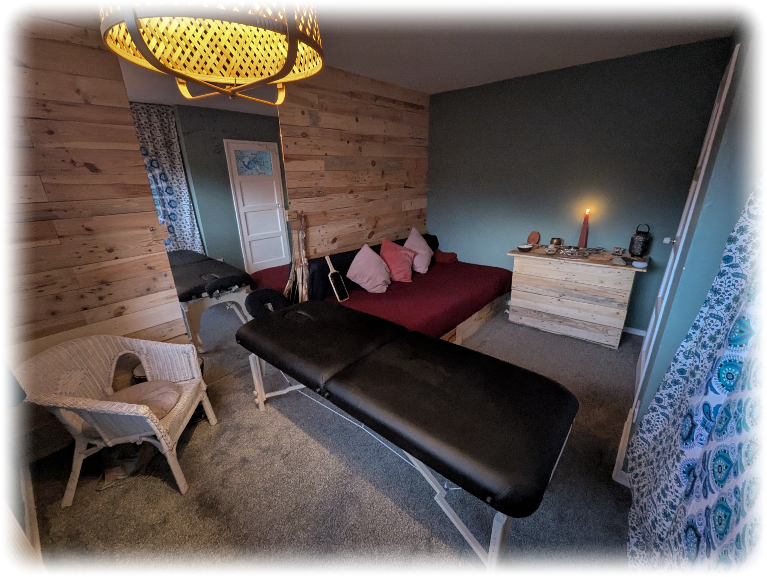A cosy, candlelit therapy room for tantric massage and shadow work, featuring a professional massage table, red daybed, and rustic wooden décor.